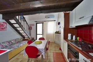 Wohnzimmer mit Küchenzeile, Schlafcouch, Essbereich und Aufgang zur Mansarde in den Ferienhäusern Turagri an der Costa Rei, Sardinien