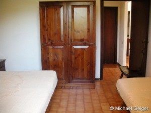 Schlafzimmer mit Doppelbett und einem Einzelbett mit Blick auf den Schrank in den Ferienwohnungen Ginster an der Costa Rei, Sardinien